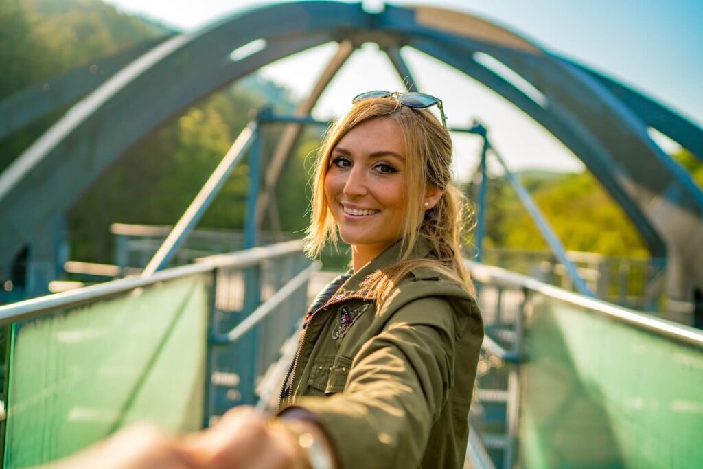 Frau steht auf dem Glassteg des Baumwipfelpfads mit Ausblick ins Tal