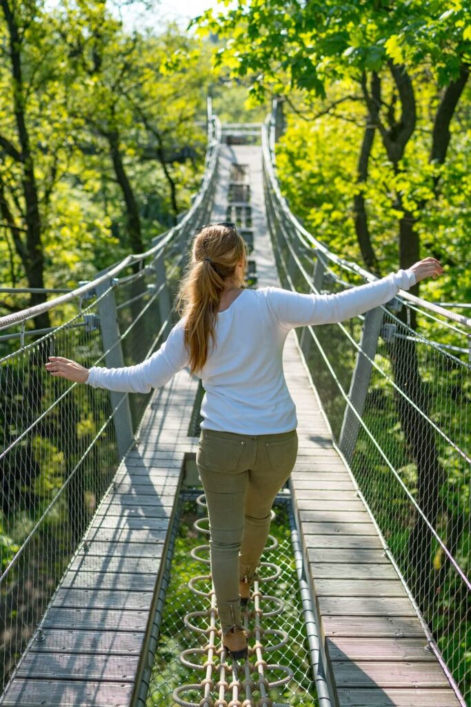 Frau balanciert über die Hängebrücke des Baumwipfelpfads an einem sonnigen Tag